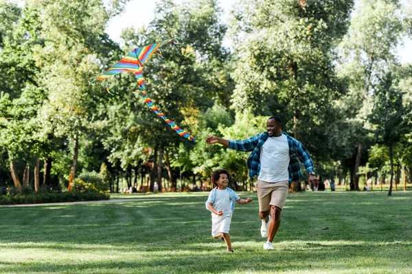 公園で父と凧と一緒に走っている幸せなアフリカ系アメリカ人の子供 — ストック写真