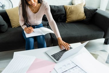 evrak yapıyor ve dizüstü bilgisayar kullanarak gülümseyen Afrikalı Amerikalı kadın kırpılmış görünümü 