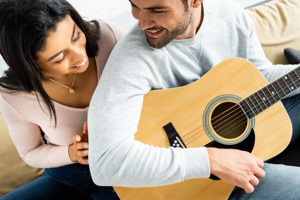 smiling african american woman looking at man with acoustic guitar