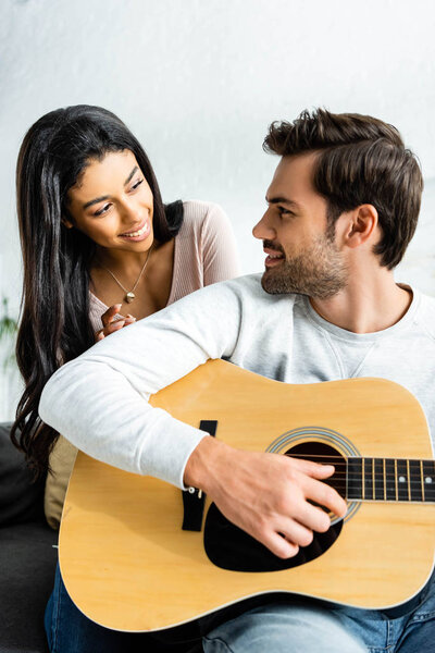 smiling african american woman looking at man with acoustic guitar