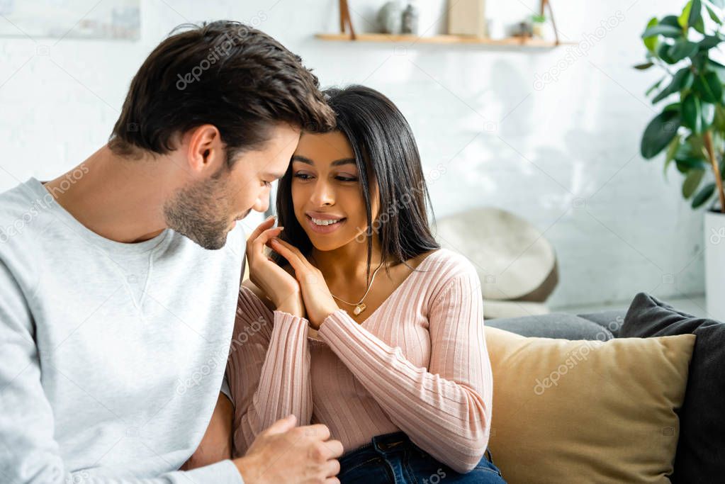 smiling african american woman looking at her boyfriend in apartment 