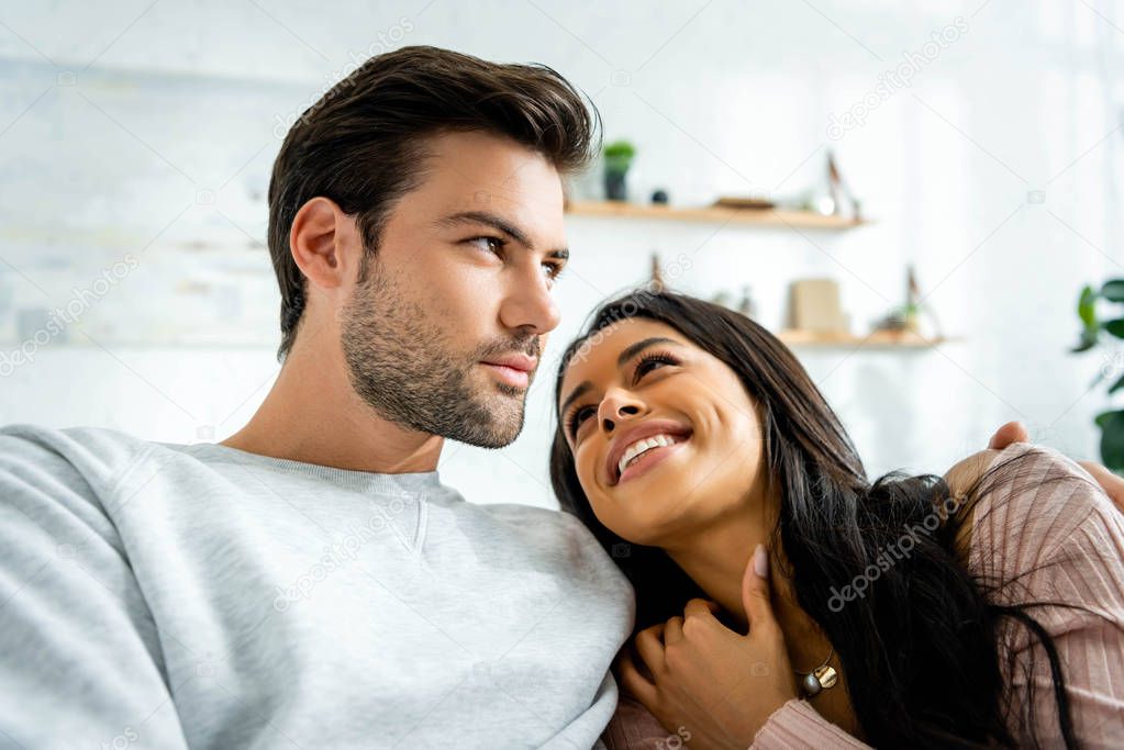 african american woman and handsome man smiling and hugging in apartment 