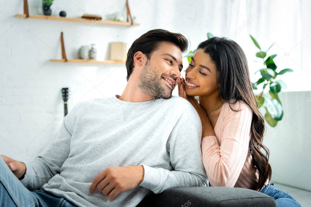 african american woman and handsome man smiling and looking at each other in apartment 