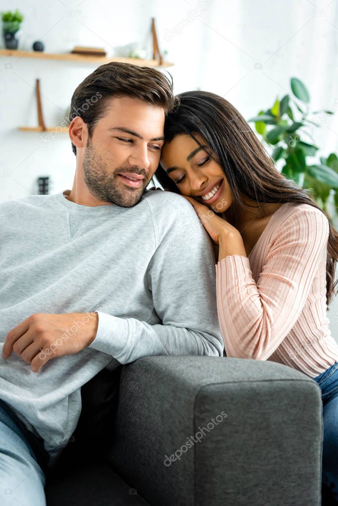 african american woman and handsome man smiling and hugging in apartment 