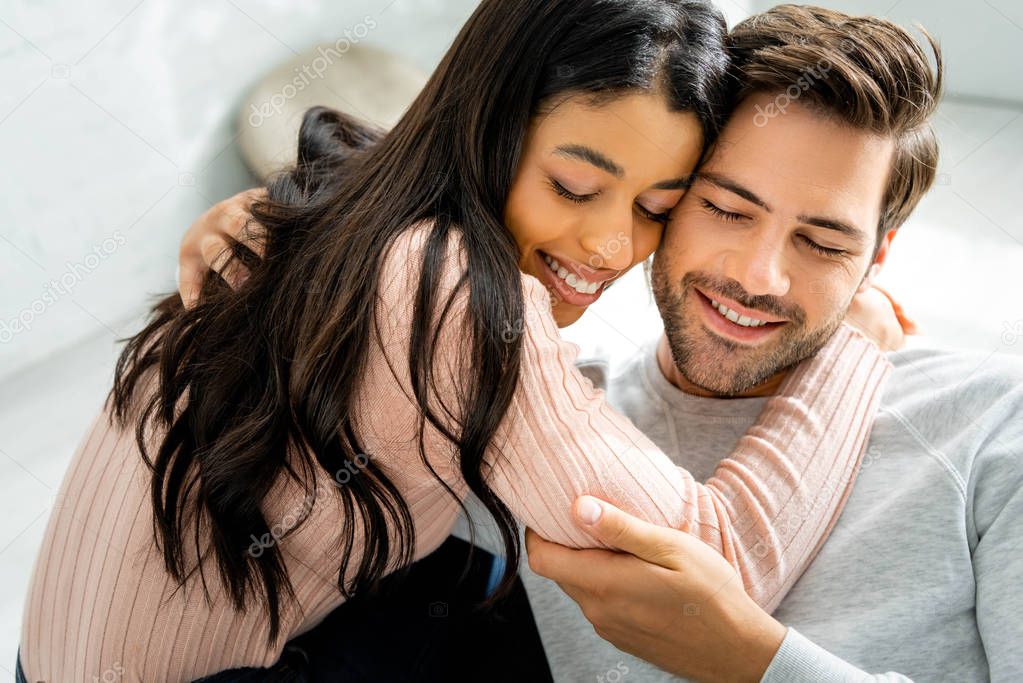 african american woman and handsome man smiling and hugging in apartment 