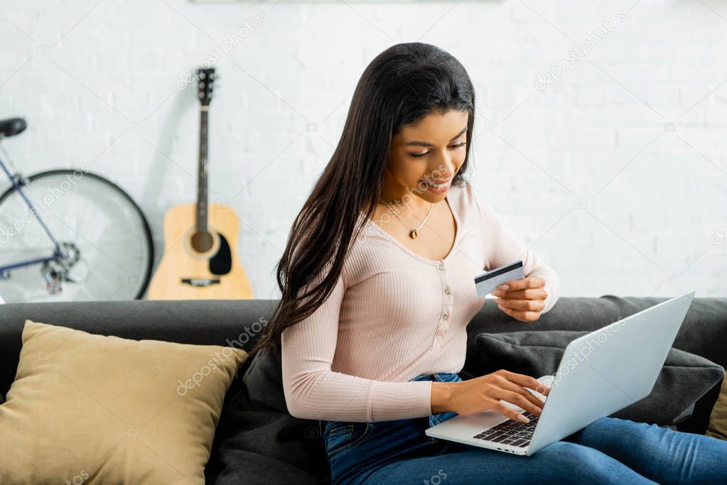 smiling african american woman holding credit card and using laptop 