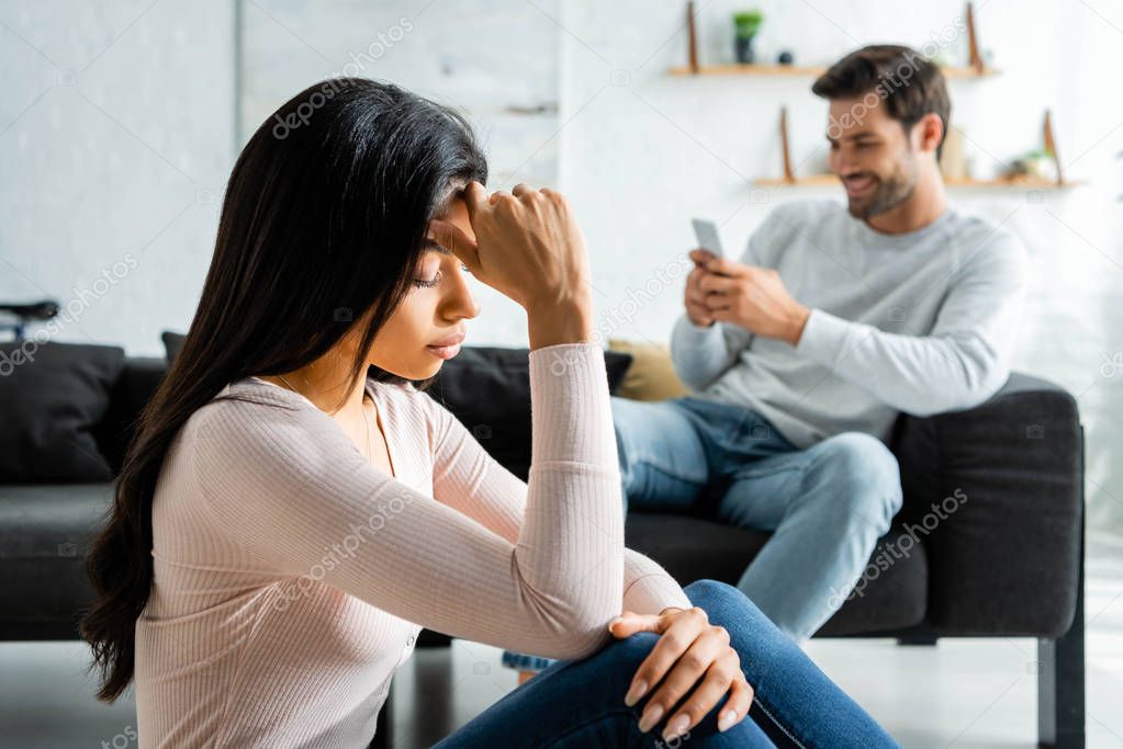 selective focus of sad african american woman and man using smartphone 