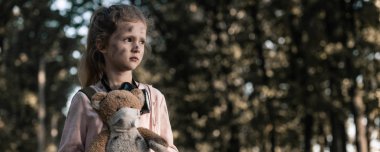 panoramic shot of kid holding dirty teddy bear near trees in chernobyl, post apocalyptic concept clipart