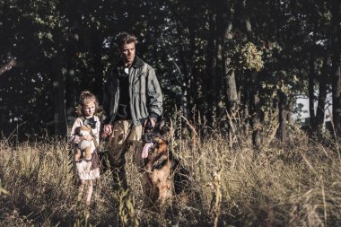 Yakışıklı bir adam çocuk ve Alman çoban köpeğiyle sahada duruyor, kıyamet sonrası konsepti.