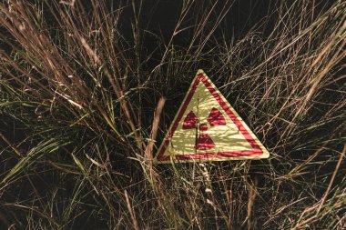 Çimenlerin üzerinde toksik uyarı sembolü olan üçgenin üst görünümü, kıyamet sonrası kavramı