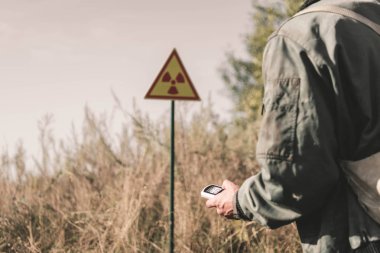 cropped view of man holding radiometer near toxic symbol, post apocalyptic concept clipart