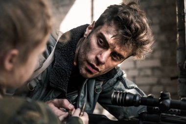 selective focus of handsome man with gun looking at kid with bullet, post apocalyptic concept clipart