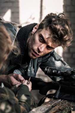 selective focus of handsome man with gun taking bullet near kid, post apocalyptic concept clipart