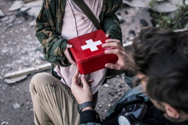 cropped view of kid giving first aid kid to man, post apocalyptic concept clipart