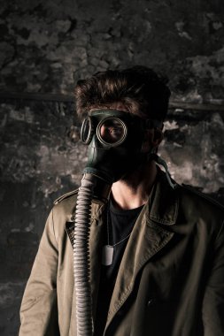 Gaz maskeli adam eski odada yıpranmış duvarın yanında duruyor, kıyamet sonrası konsepti.