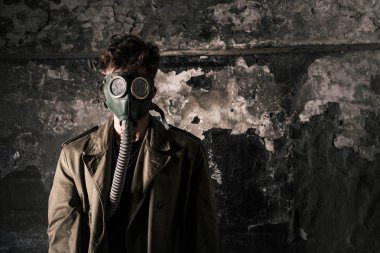 Gaz maskeli adam yıpranmış duvarın yanında duruyor, kıyamet sonrası konsepti.