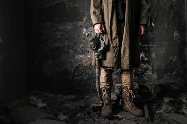 Terk edilmiş bir odada eski duvarın yanında duran adamın gaz maskesi, kıyamet sonrası konsepti.