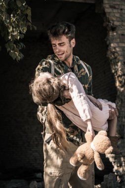 Üzgün adam elinde oyuncak ayıyla silah tutuyor, kıyamet sonrası konsepti.