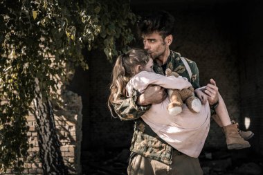 handsome man holding in arms and kissing kid with teddy bear, post apocalyptic concept clipart