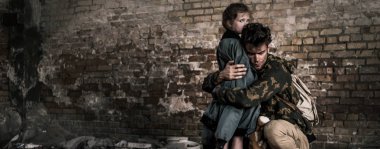 panoramic shot of handsome man hugging child near brick wall, post apocalyptic concept clipart