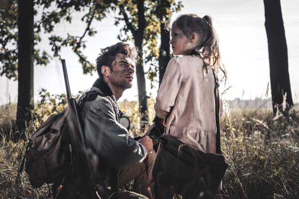 handsome man looking at dirty kid in field, post apocalyptic concept