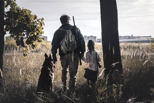 back view man standing in field with kid and german shepherd dog, post apocalyptic concept