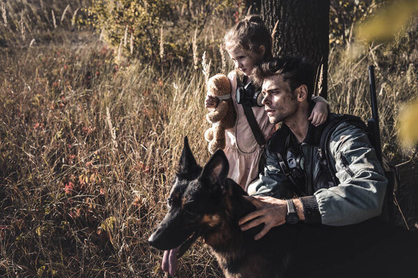 selective focus of man touching german shepherd dog near cute kid in field, post apocalyptic concept