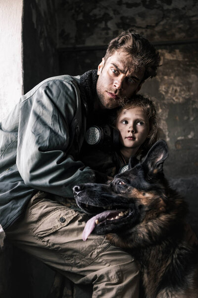 selective focus of man looking at camera near kid and german shepherd dog, post apocalyptic concept