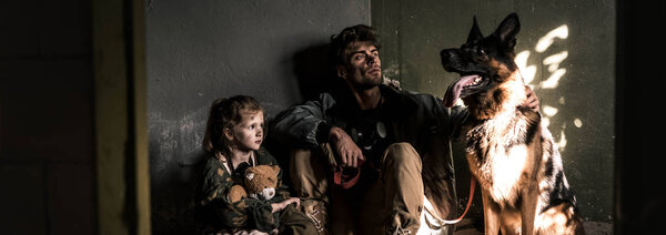 panoramic shot of man and kid sitting with german shepherd dog, post apocalyptic concept