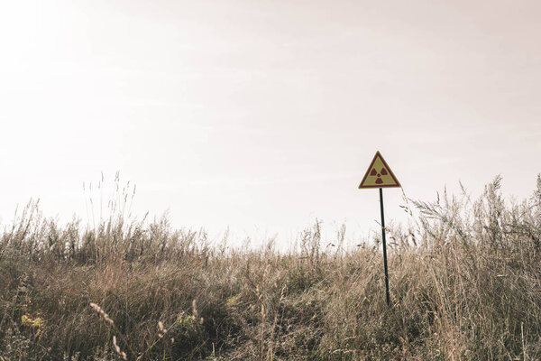 triangle with warning toxic symbol near field, post apocalyptic concept