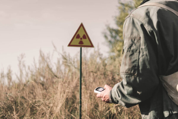 cropped view of man holding radiometer near toxic symbol, post apocalyptic concept