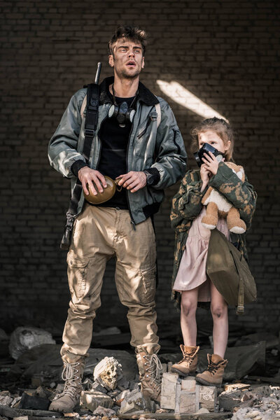 handsome man holding flask near kid in gas mask, post apocalyptic concept