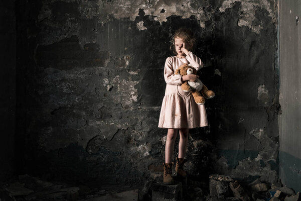 frustrated kid crying while holding teddy bear in dirty room, post apocalyptic concept