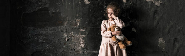 panoramic shot of frustrated kid crying while holding teddy bear in dirty room, post apocalyptic concept