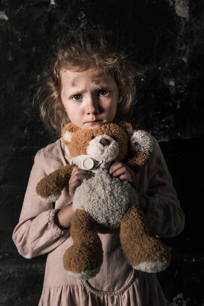 frustrated kid holding teddy bear in dirty room, post apocalyptic concept