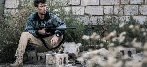 panoramic shot of handsome man with gun near brick wall outside, post apocalyptic concept