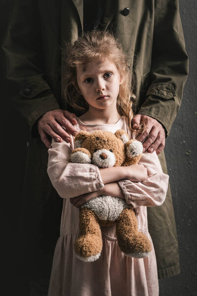 cropped view of man standing near kid with teddy bear, post apocalyptic concept