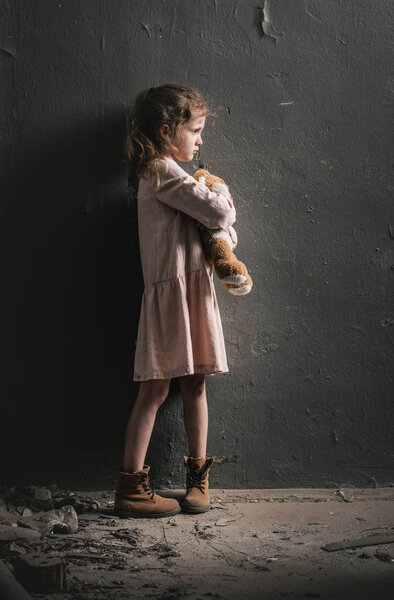 side view of kid holding soft toy near wall, post apocalyptic concept