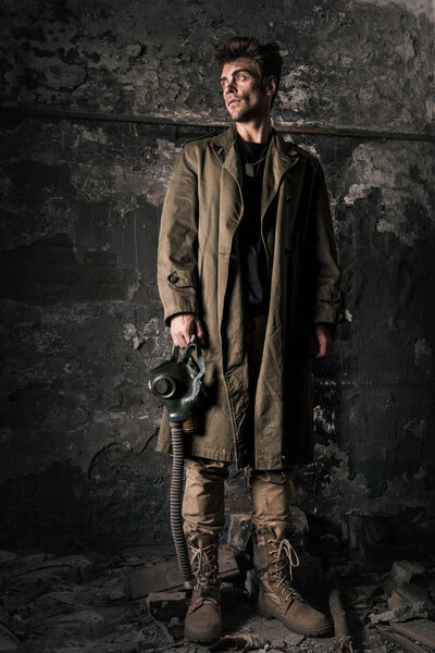 handsome man standing near old wall with gas mask, post apocalyptic concept