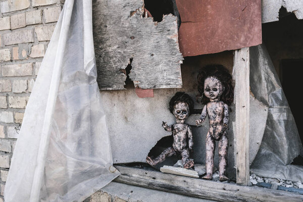 scary and burnt baby dolls near rusty window, post apocalyptic concept
