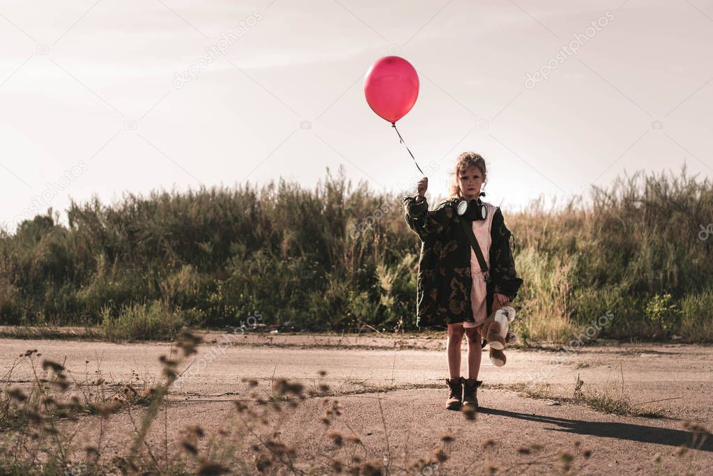 selective focus of cute kid with gas mask holding balloon, post apocalyptic concept