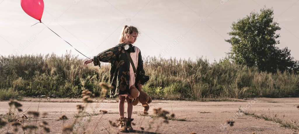 panoramic shot of cute child with gas mask holding balloon, post apocalyptic concept