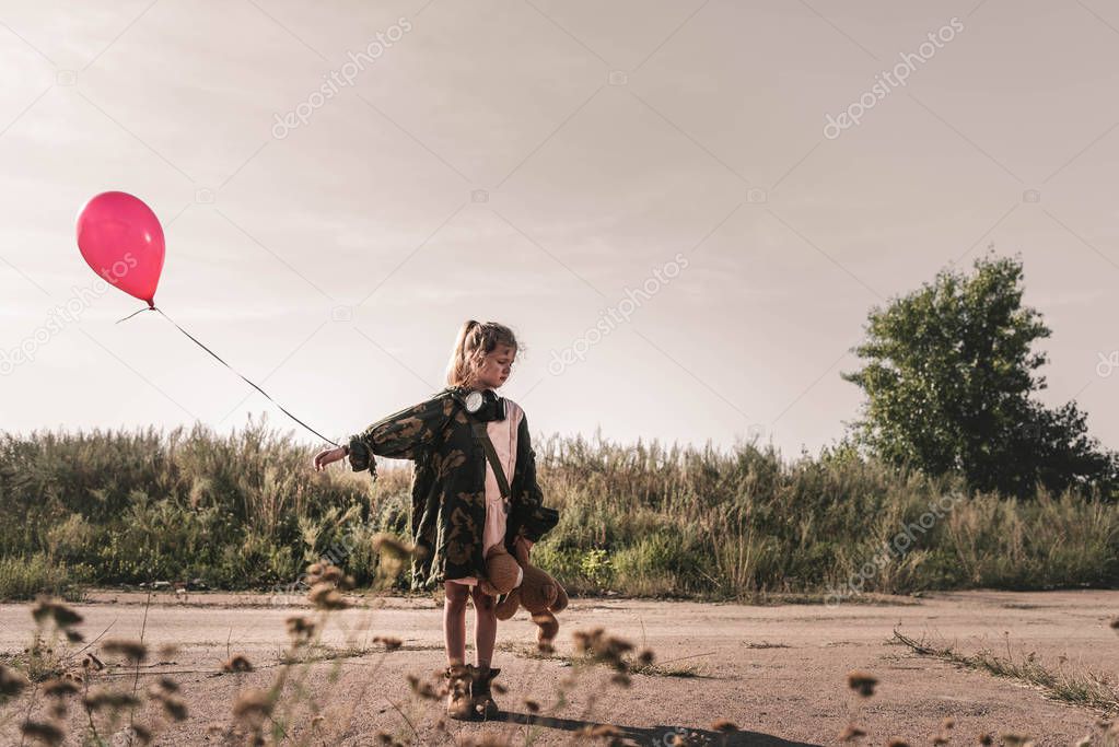 selective focus of cute kid with gas mask holding balloon, post apocalyptic concept