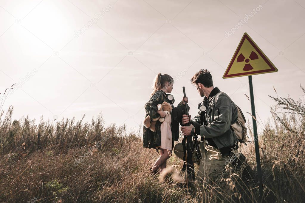 handsome man with gun near kid with teddy bear and toxic symbol, post apocalyptic concept