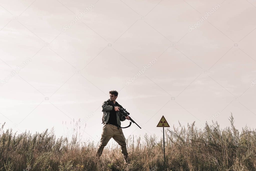  man holding gun near toxic symbol in field, post apocalyptic concept