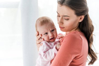 Çekici bir kadın kollarında ağlayan bir bebeği evde tutuyor. 