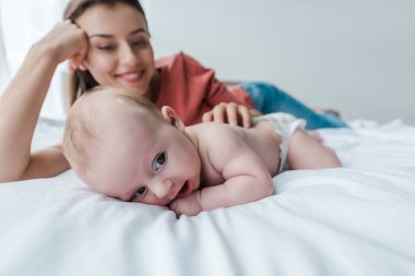Yatak odasında neşeli bir annenin yanında sevimli bir bebeğin seçici odağı. 