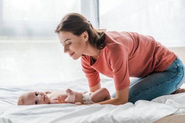 Mutlu anne tatlı bebeğe dokunuyor. Yatakta yatıyor. 