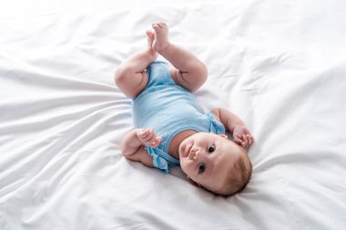 Mavi bebek tulumu giymiş şirin bir bebek evde yatakta yatıyor. 