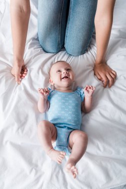 Pantolonlu annenin mavi bebek tulumunun içinde mutlu bir bebeğin yanında oturduğu görüntüler. 